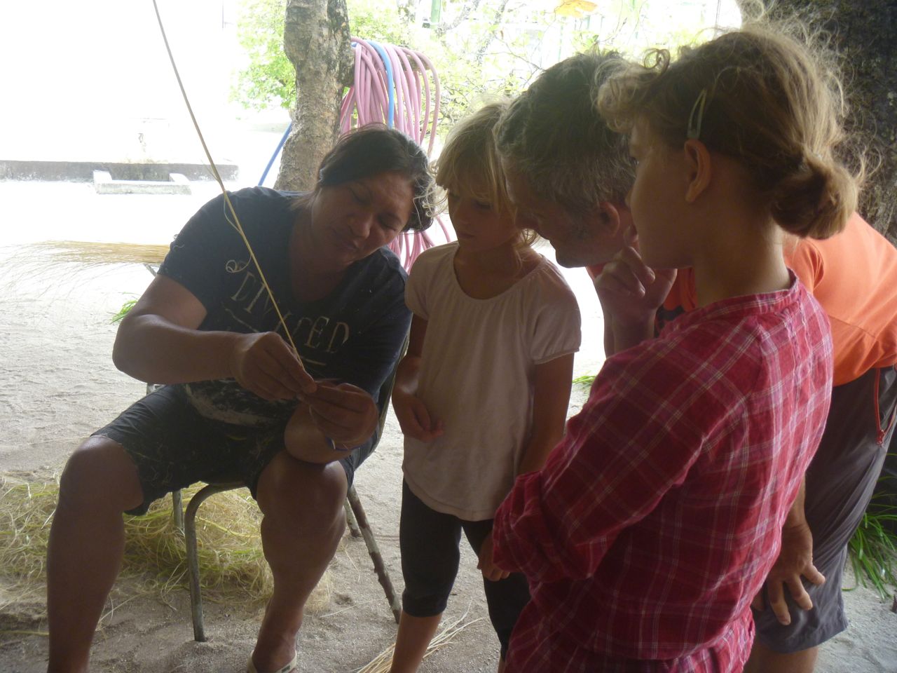 Eine Frau zeigt den Kindern, wie man die Borsten für einen Besen aus Palmenblättern herstellt.